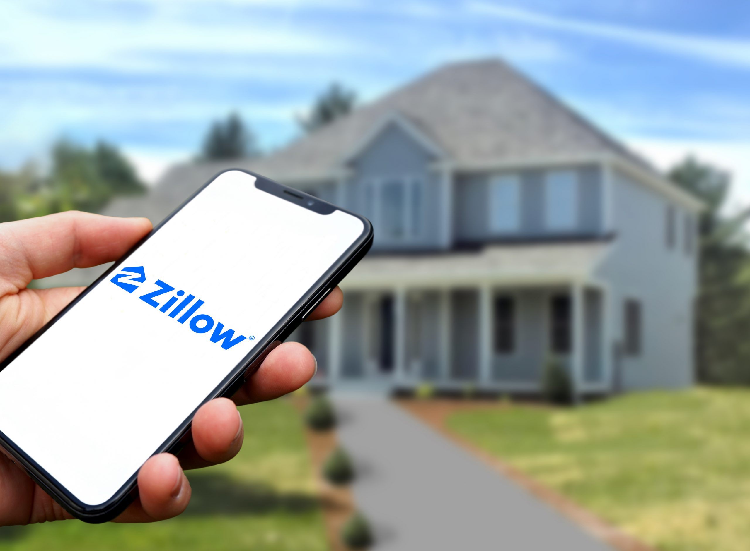 Zillow logo is displayed on a smartphone in the hand of a person