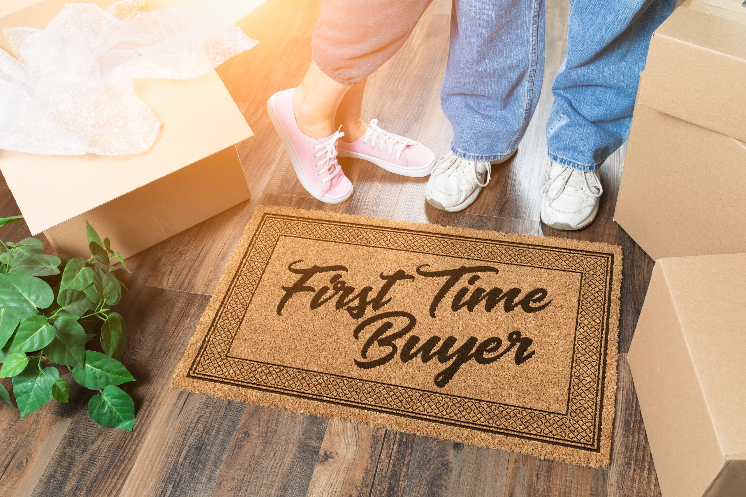 Man and Woman Unpacking Near a First Time Buyer Welcome Mat, Moving Boxes and Plant.